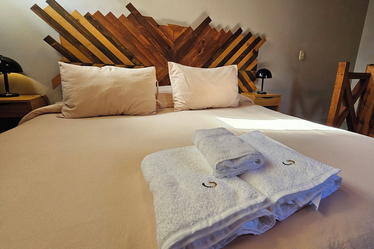Een net opgemaakt bed met twee kussens, een houten hoofdbord en twee opgerolde handdoeken op het bed.