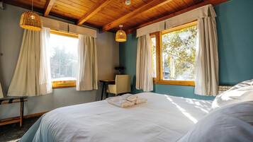 Une chambre avec un grand lit, deux fenêtres avec des rideaux, un bureau et une chaise.