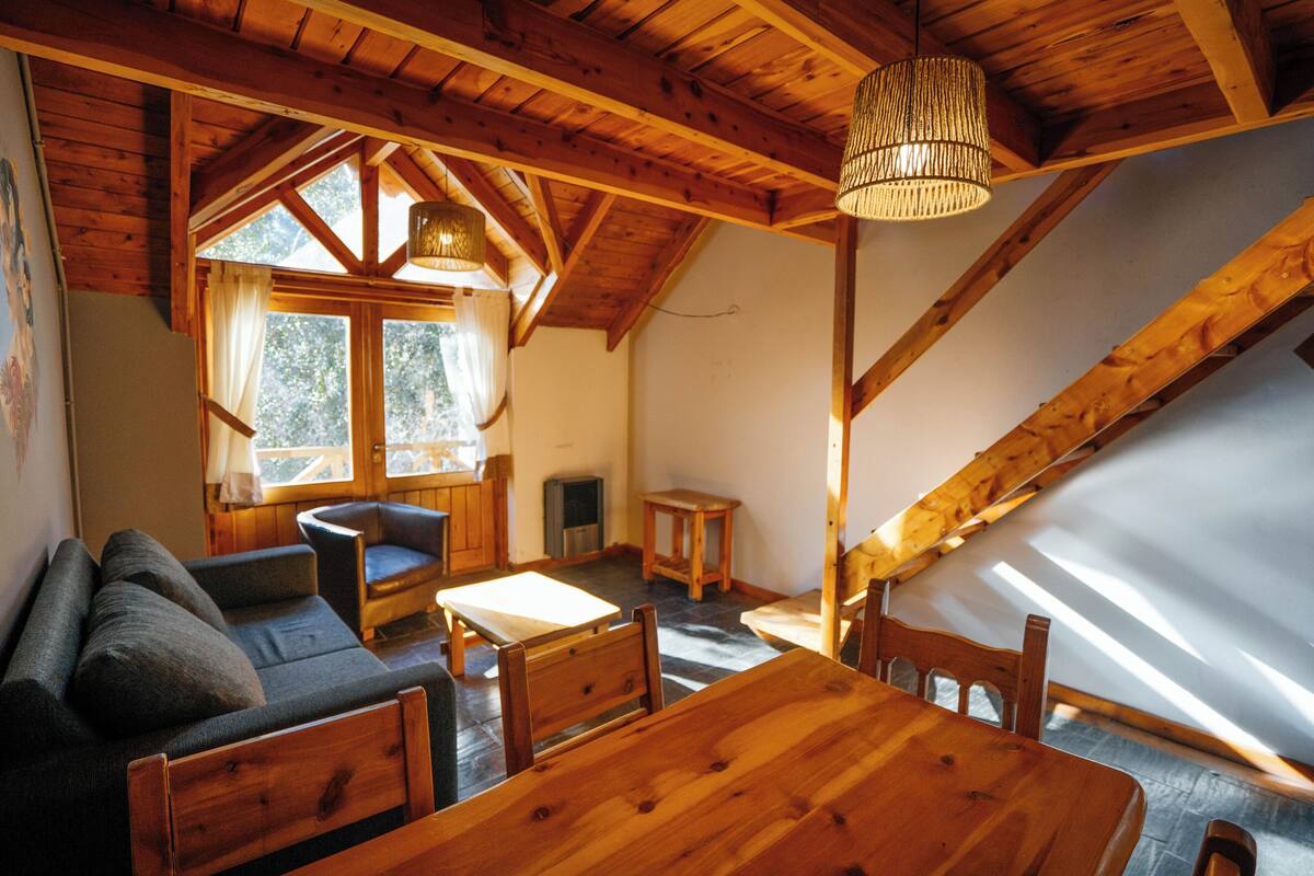 Une pièce chaleureuse avec un plafond en bois, un canapé, une table à manger et une fenêtre avec des rideaux.