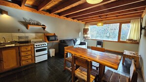Uma cozinha rústica com armários de madeira, fogão, micro-ondas e uma mesa de jantar com bancos.