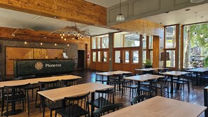 Interior de restaurante con vigas de madera, mostrador de recepción y varias mesas y sillas.