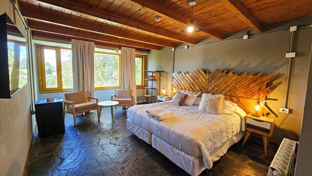 Un dormitorio acogedor con una cama grande, dos sillas, una mesita y un cabecero de madera.