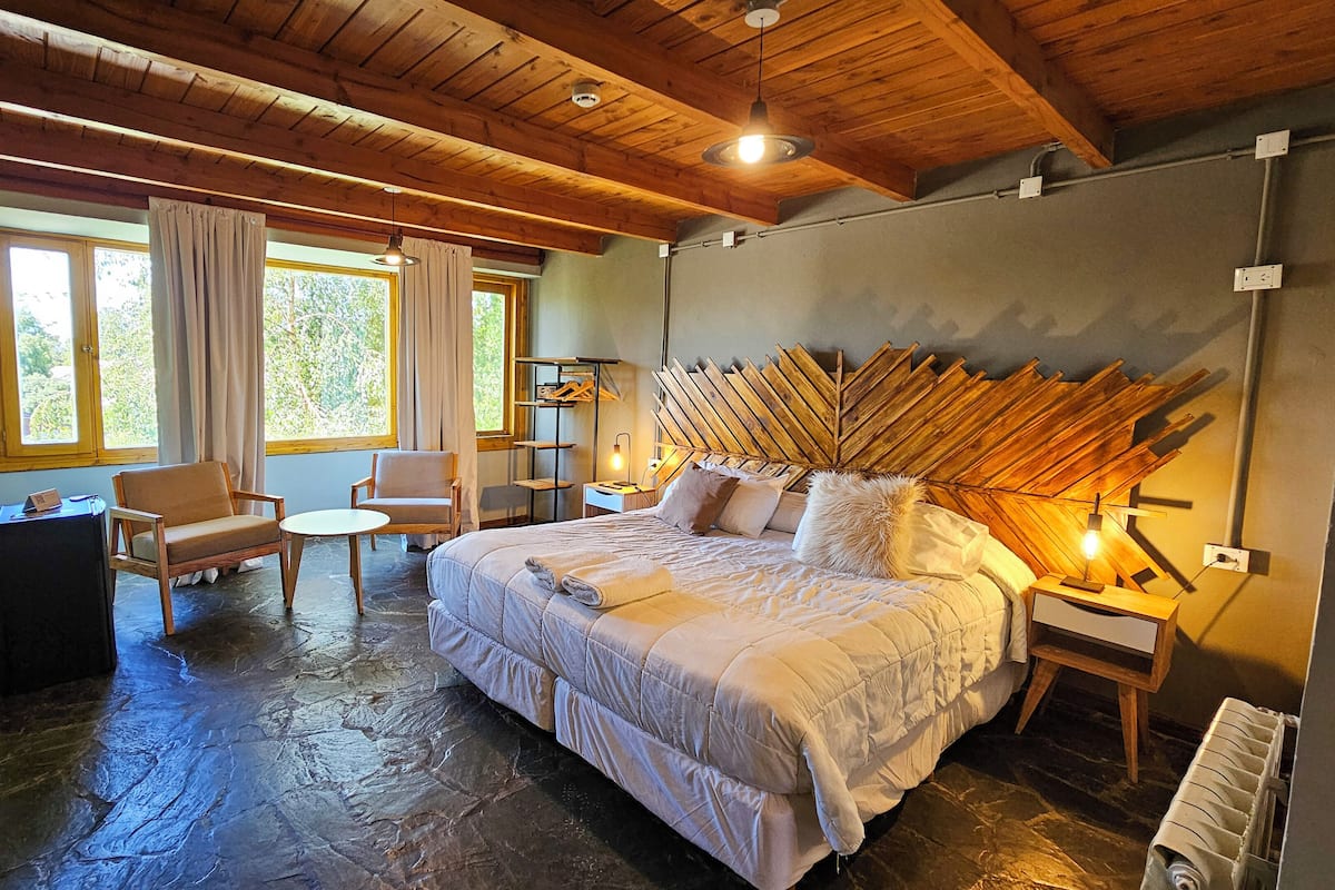 Une chambre confortable avec un grand lit, deux fauteuils, une petite table et une tête de lit en bois.