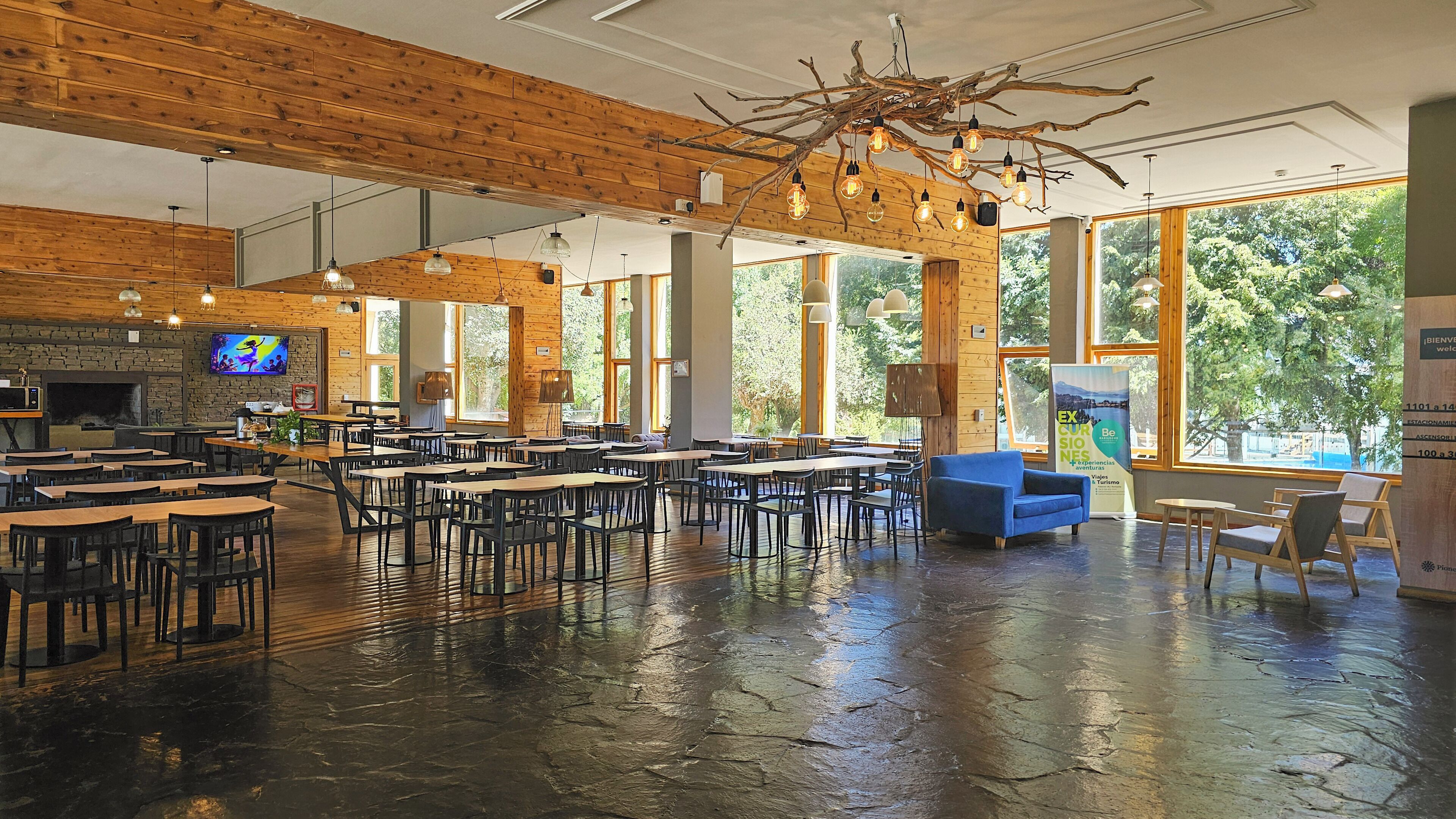 A spacious indoor area with wooden walls and large windows, featuring tables and chairs arranged for dining or meetings.