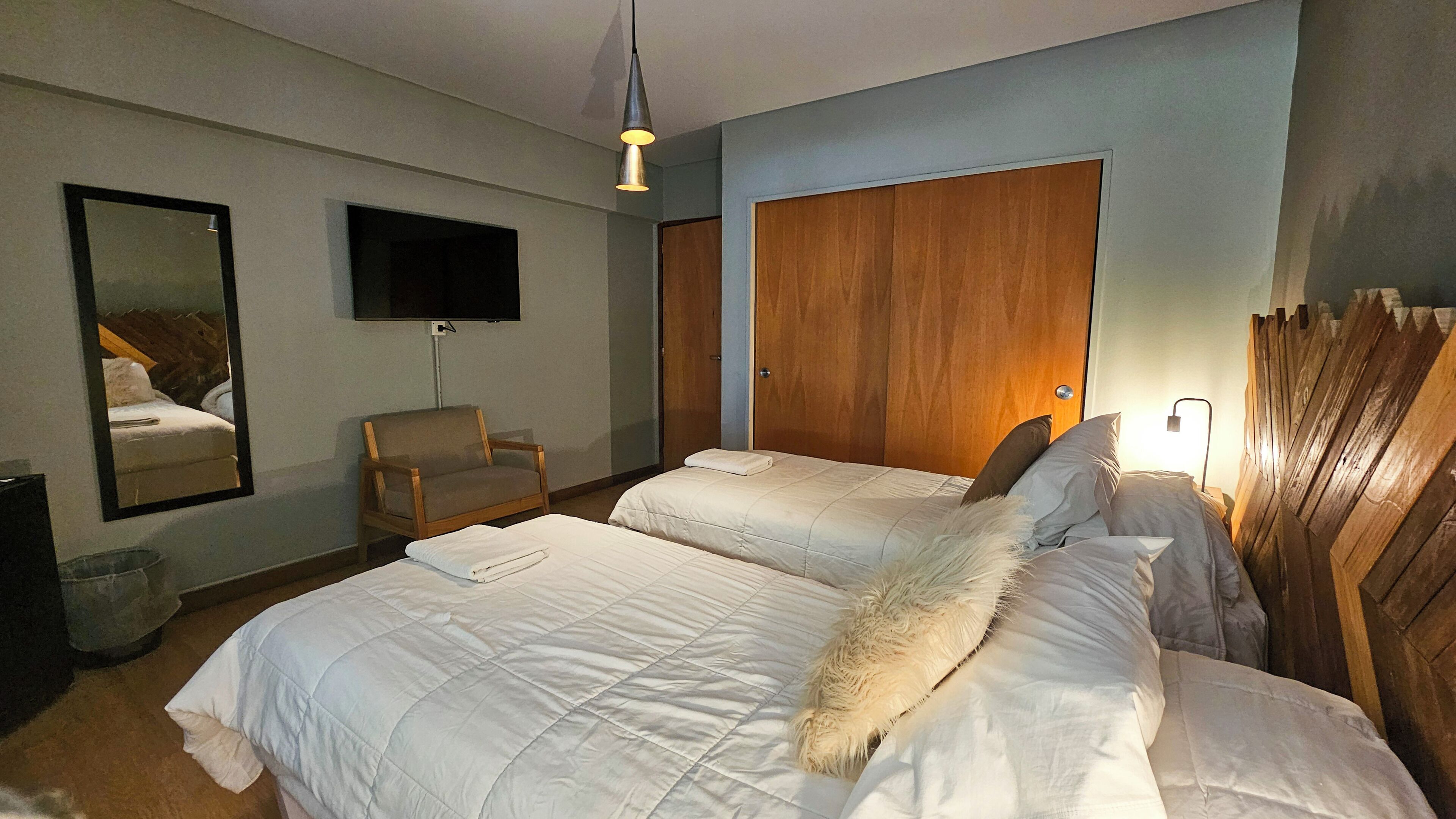 Een hotelkamer met twee bedden, een houten garderobe, een stoel, een televisie en een spiegel.
