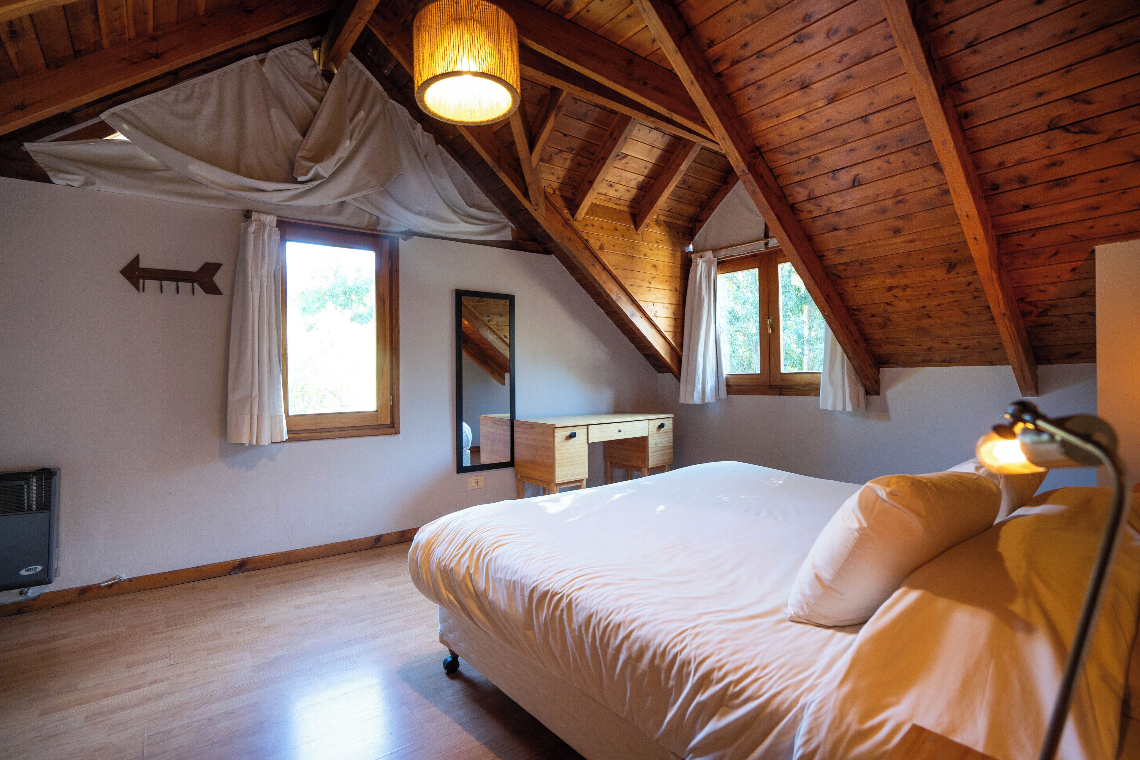 A bedroom with a wooden ceiling, a bed, a desk, and a mirror.