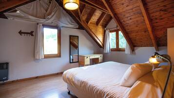 A bedroom with a wooden ceiling, a bed, a desk, and a mirror.