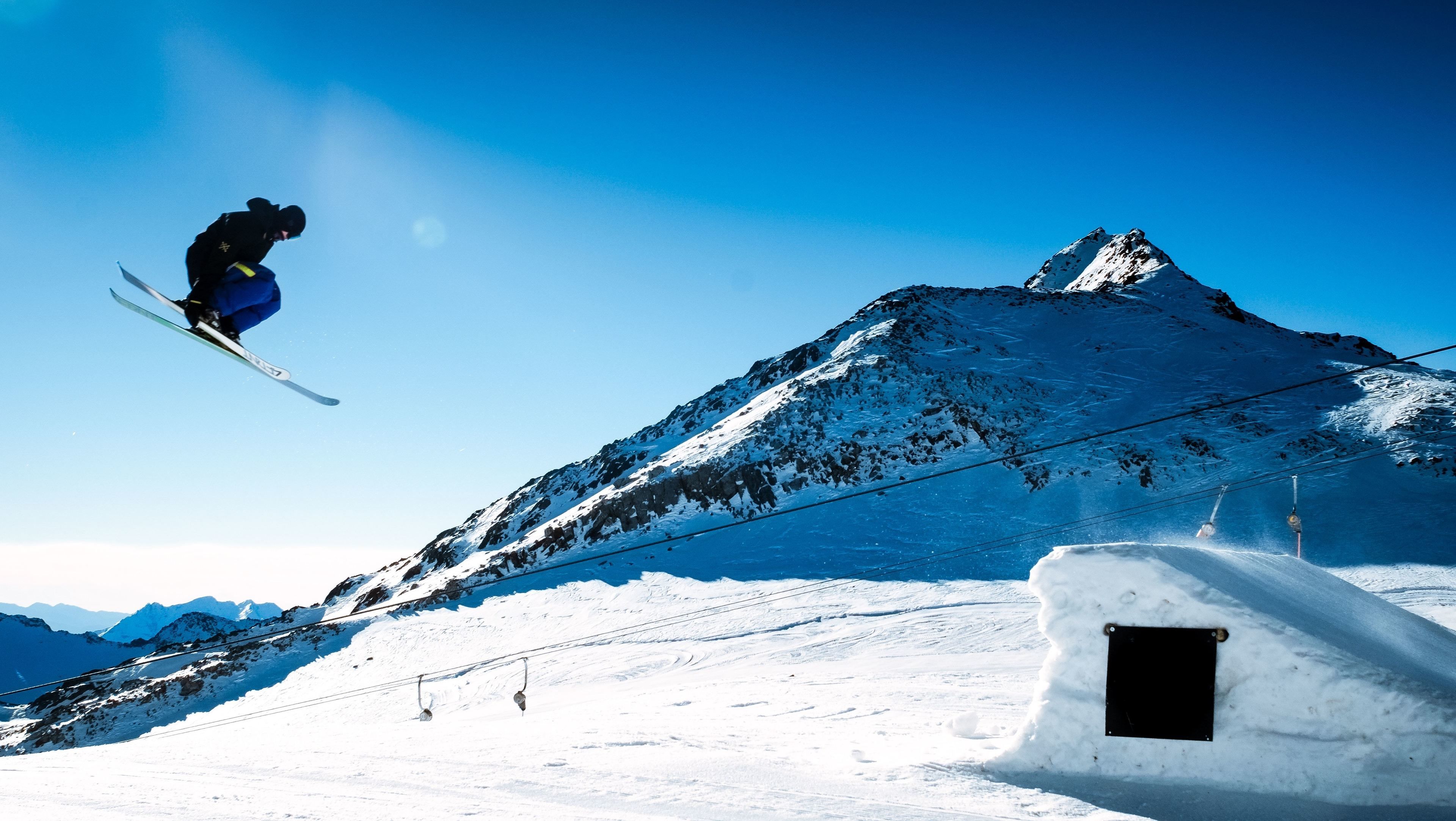 A ski jump with a clear sky and a snow-covered mountain in the background.