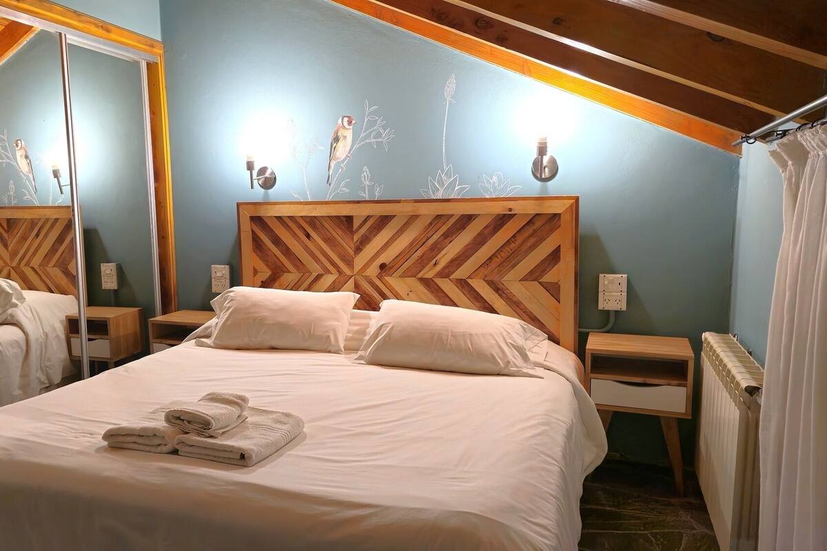 Une chambre à coucher avec une tête de lit en bois, un lit avec du linge de lit blanc, un miroir, des tables de chevet et un radiateur.