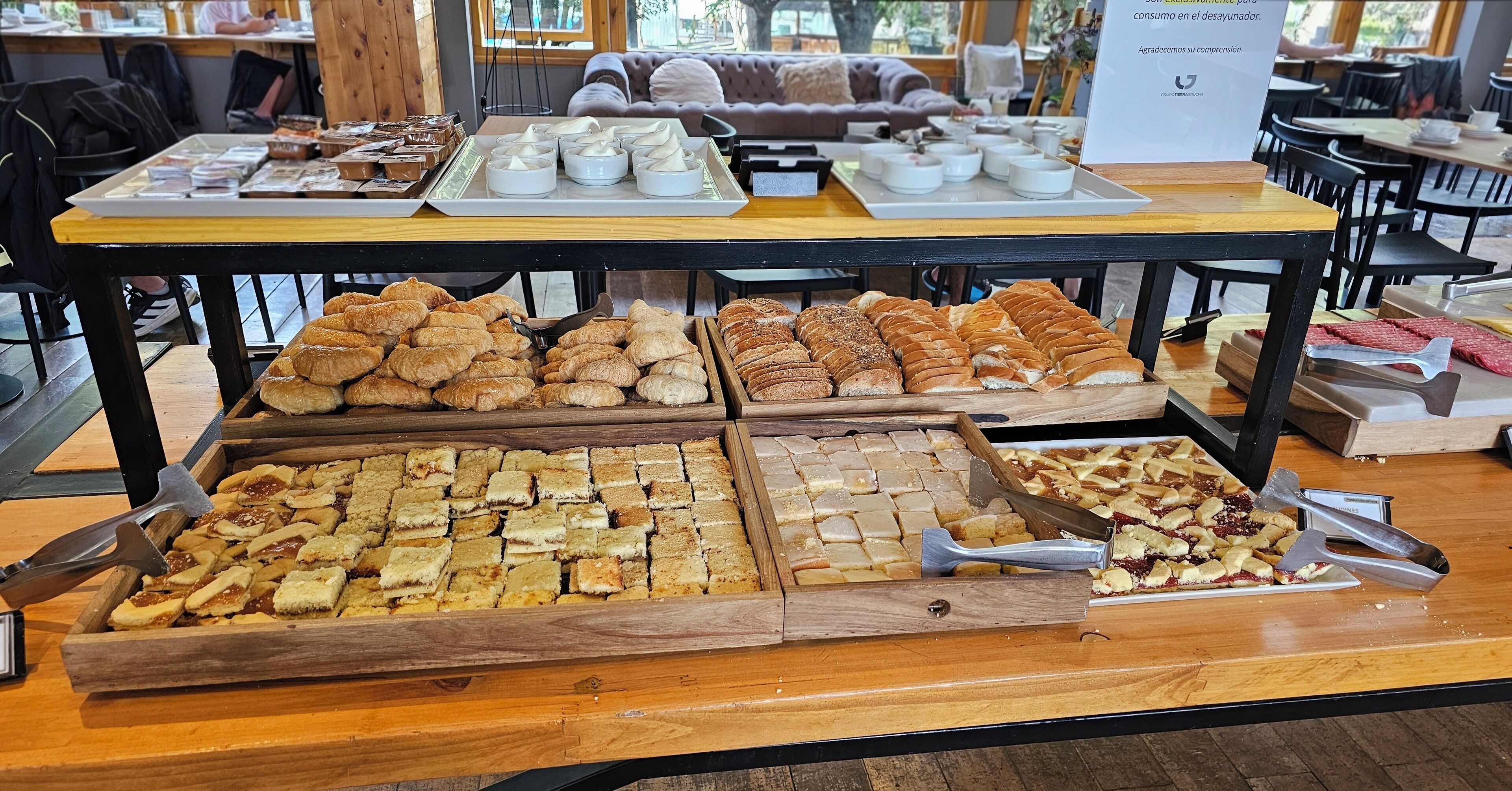 Una mesa de buffet con diversos pasteles y postres, incluyendo croissants y tartas, en un ambiente de cafetería.