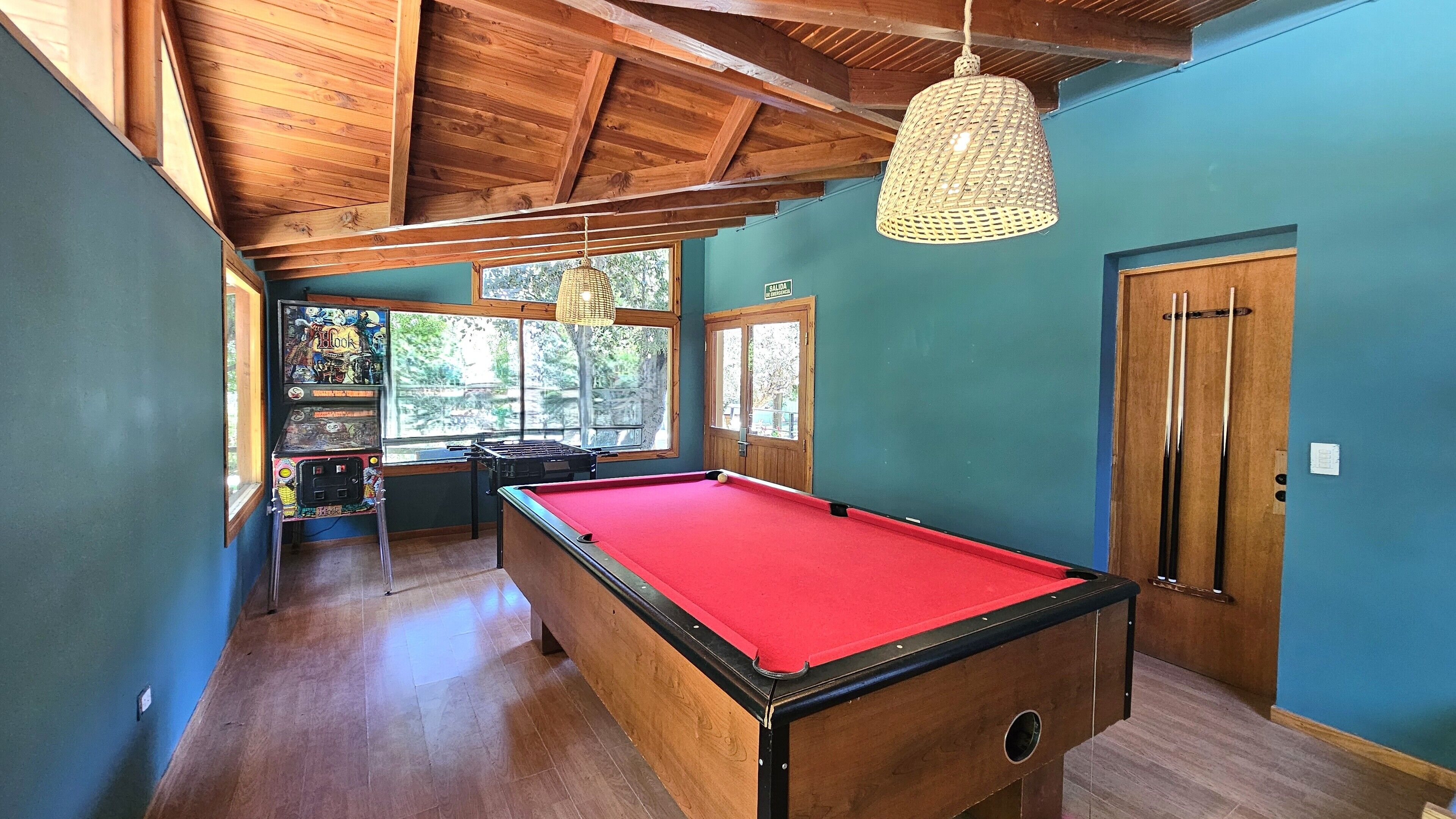 A pool table in a room with wooden beams, a billiards rack, and a door labeled "SALIDA".