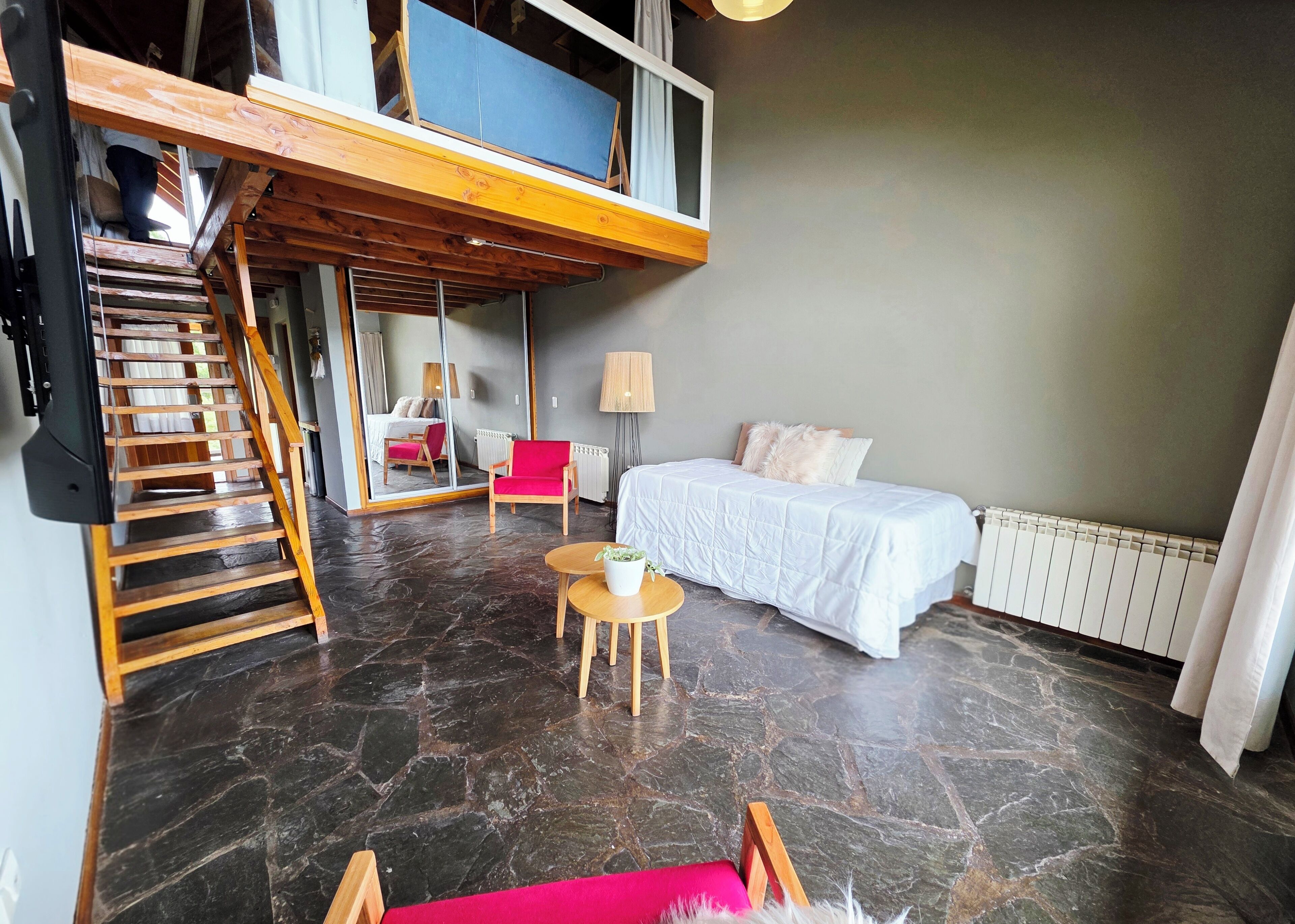 Een moderne kamer met een bed, een rode stoel, een tafeltje, een lamp en een trap naar een hoger niveau.
