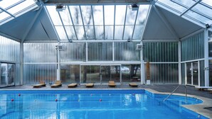 Una piscina con sillones de descanso y una estructura de techo de cristal.