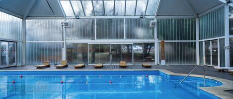 A swimming pool with lounge chairs and a glass roof structure.
