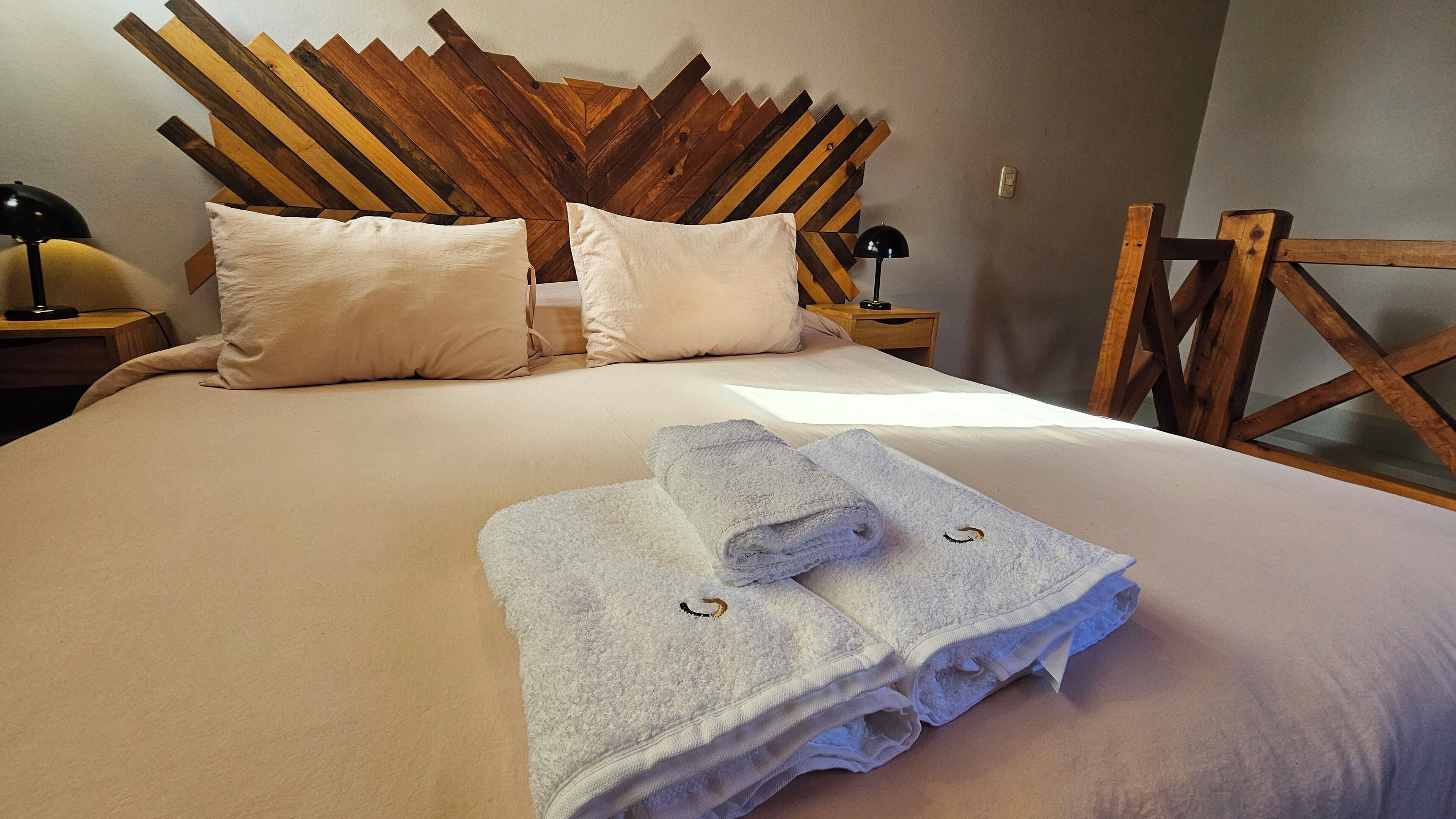 Una cama bien hecha con dos almohadas, cabecera de madera y dos toallas enrolladas sobre la cama.