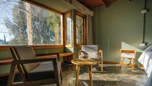 Una habitación con suelo de piedra, dos sillas de madera, una mesita redonda y una cama.