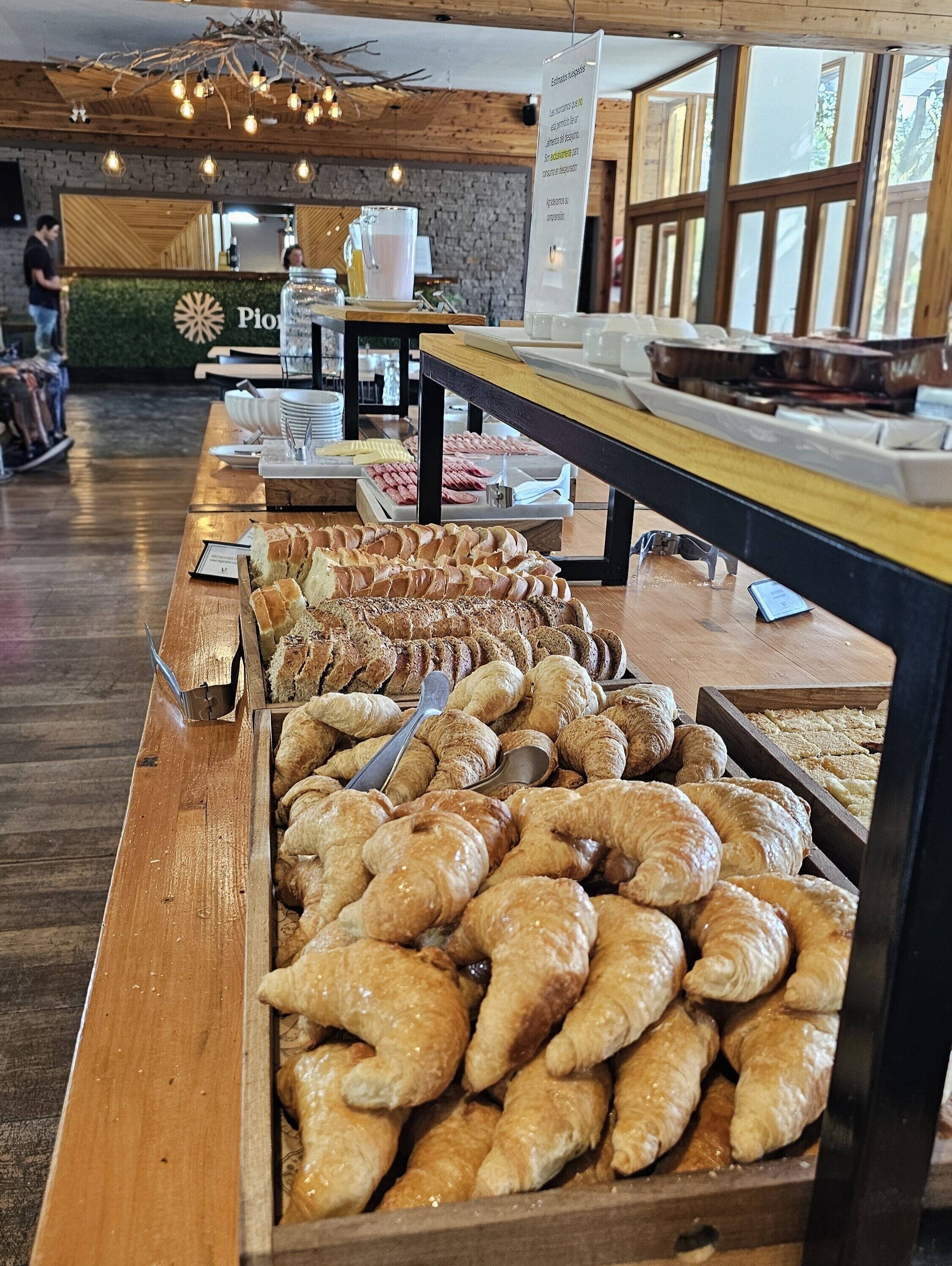 Una vetrina di panetteria con diversi dolci e pane, tavoli di legno e un arredamento rustico con travi a vista e pareti in mattoni.