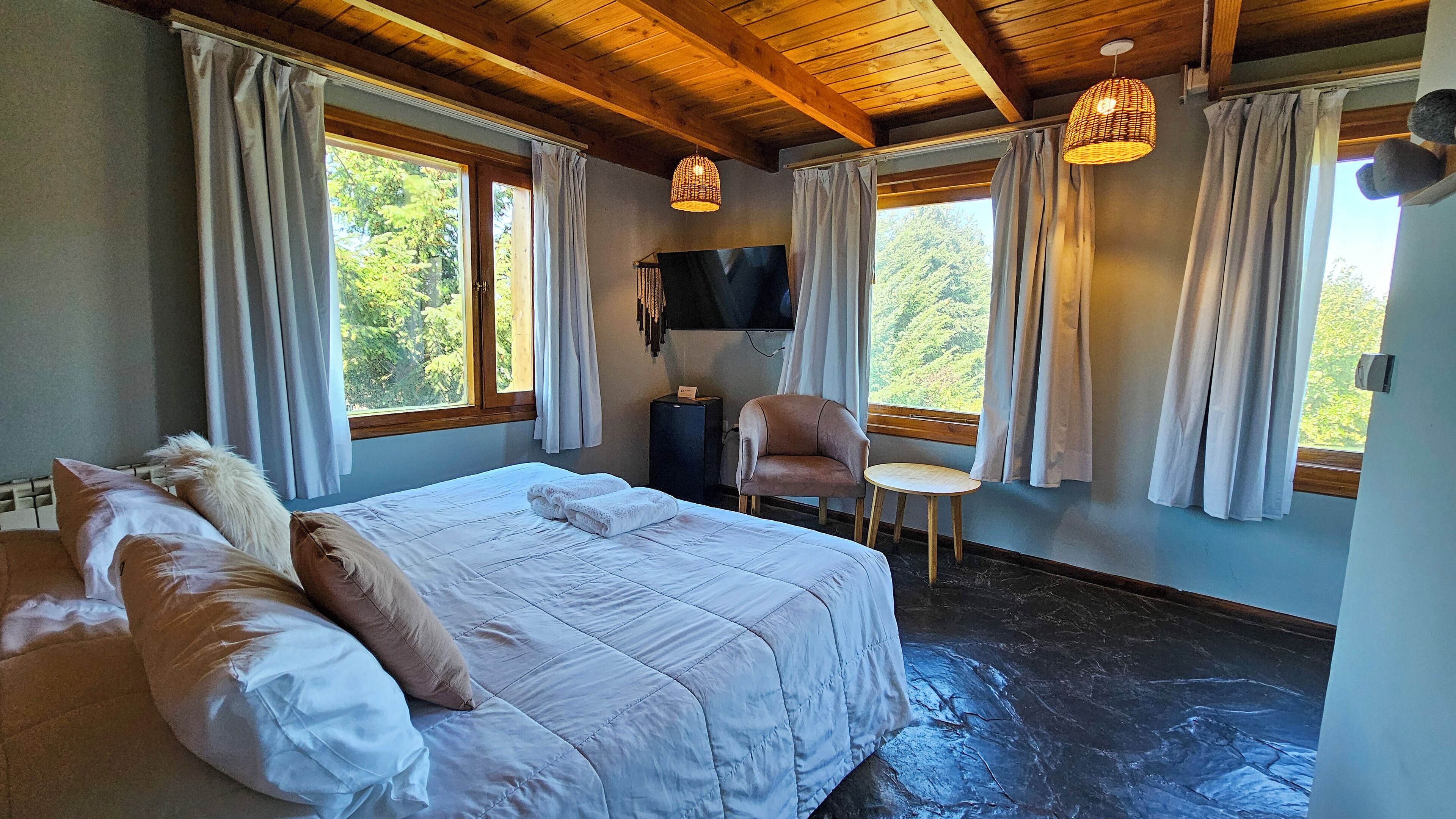 Un dormitorio con una cama grande, una silla, un televisor y una ventana con cortinas.