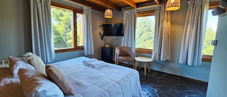 Un dormitorio con una cama grande, una silla, un televisor y una ventana con cortinas.