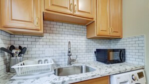 Una cocina con armarios de madera, un lavamanos de acero inoxidable, un microondas y una lavadora.