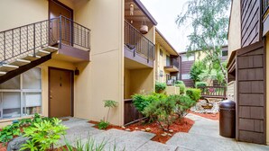 Un edificio residencial de varios pisos con un patio central, una escalera y un pequeño jardín con plantas y rocas.