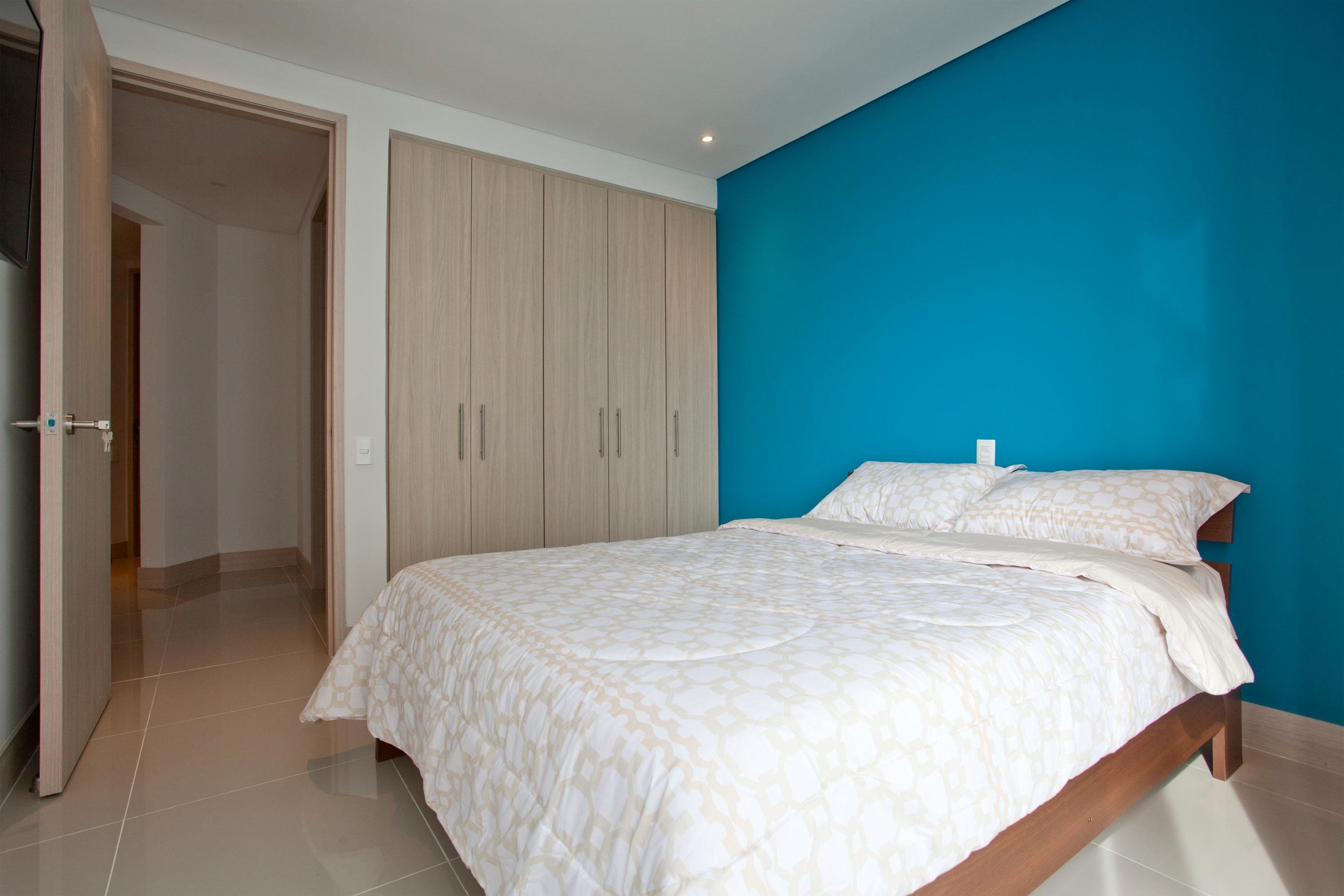 A bedroom with a bed, a wardrobe, and a blue wall.