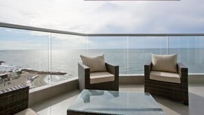 A balcony with two wicker chairs and a glass table, overlooking a beach and the sea. - Murano Elite Luxury Bocagrande (Cartagena)