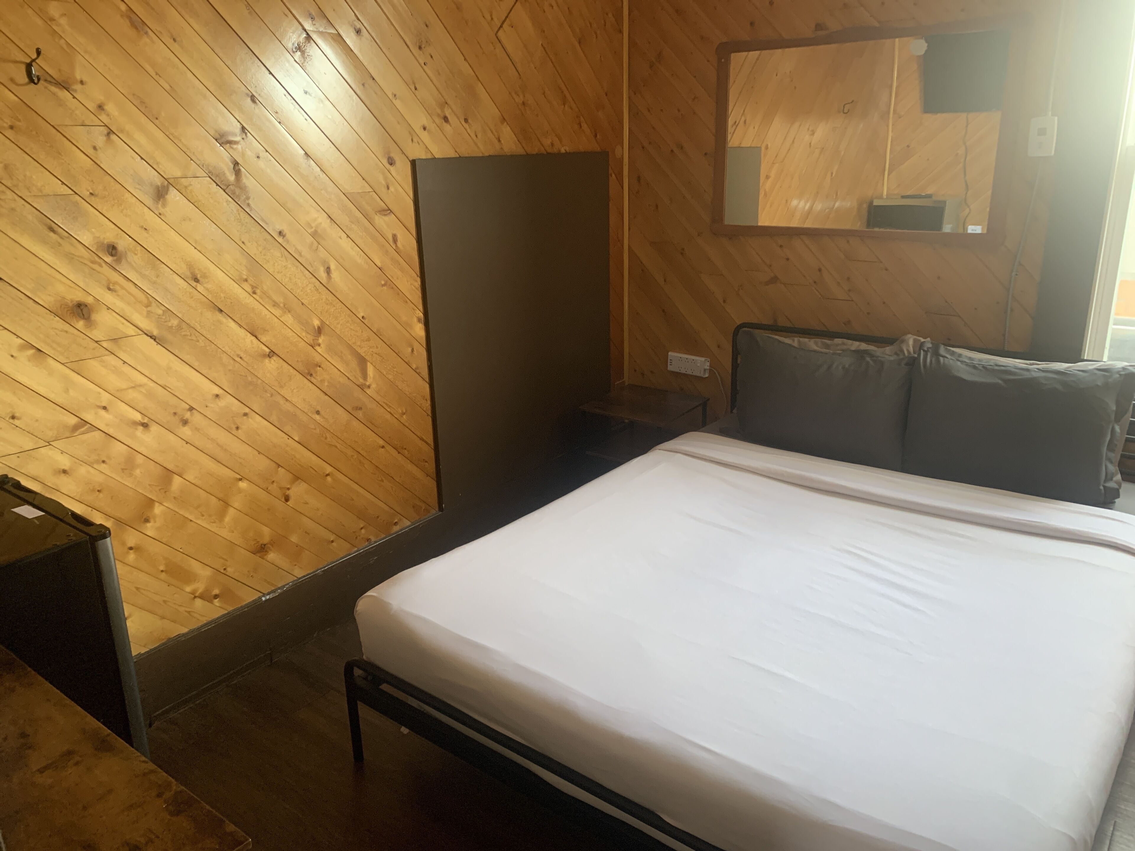 Una habitación con techo de madera inclinado, una cama con ropa de cama blanca, una mesita de noche y un espejo en la pared.