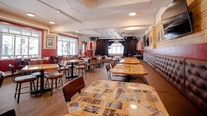 A restaurant with multiple tables and booths, large windows, and a television mounted on the wall. - Party Hostel- Canmore Hotel Hostel (Canmore)