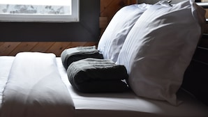A neatly made bed with white and gray linens, a window with a view, and wooden paneling on the wall. - Party Hostel- Canmore Hotel Hostel (Canmore)