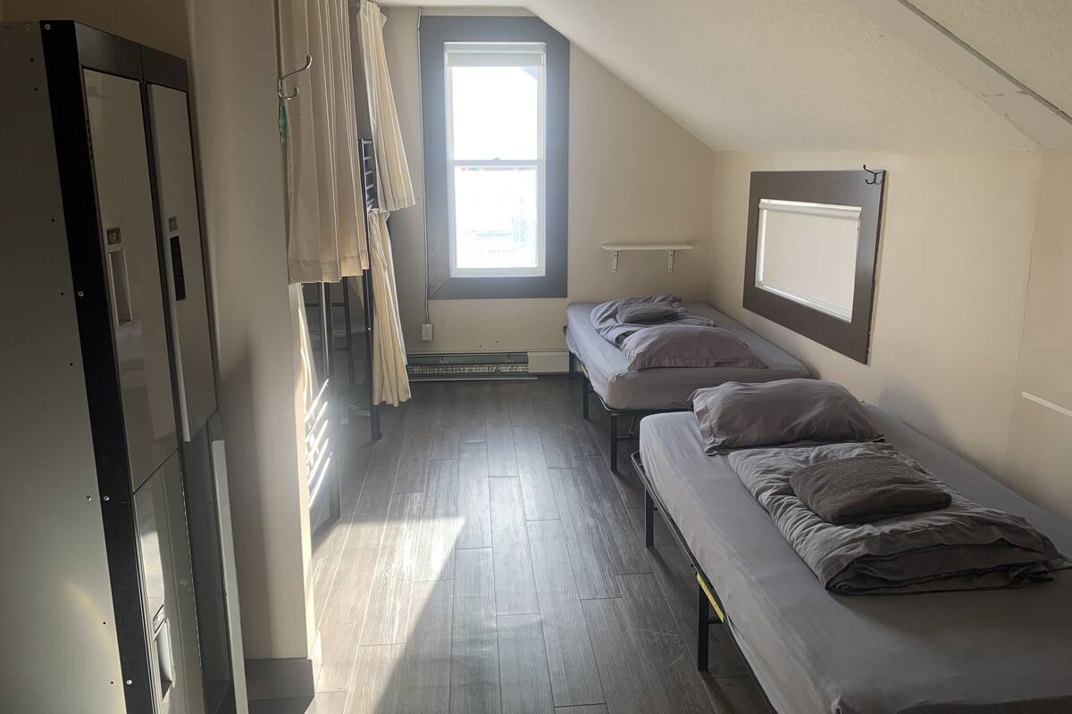 A dormitory room with two single beds, a window, a radiator, and a wardrobe.