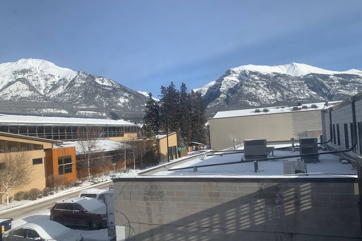 A building with a flat roof, a brick wall, and a snow-covered mountain in the background.