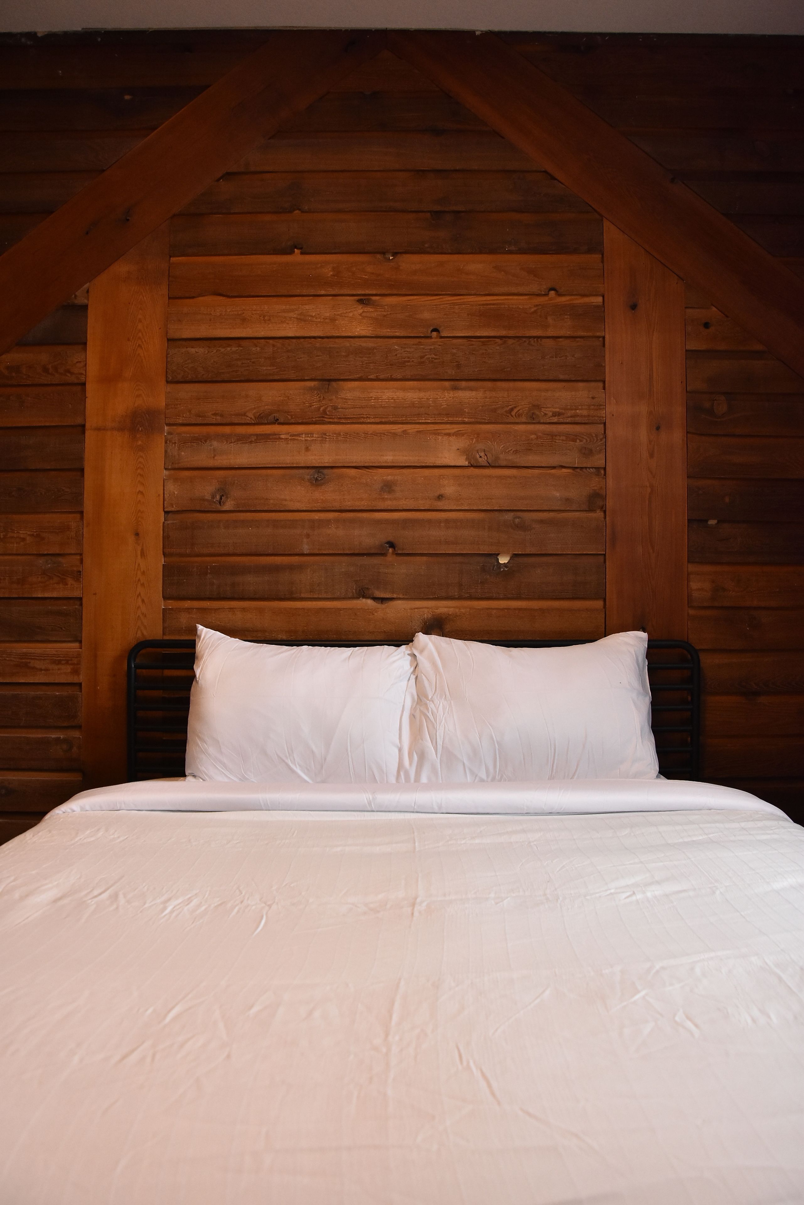A bed with white linens in a room with wooden walls and a sloped ceiling.