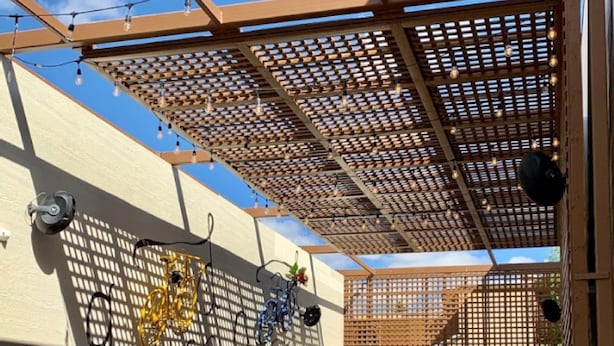 An outdoor patio with wooden tables and chairs, a bicycle, and a wall with a lattice design. - Party Hostel- Canmore Hotel Hostel (Canmore)