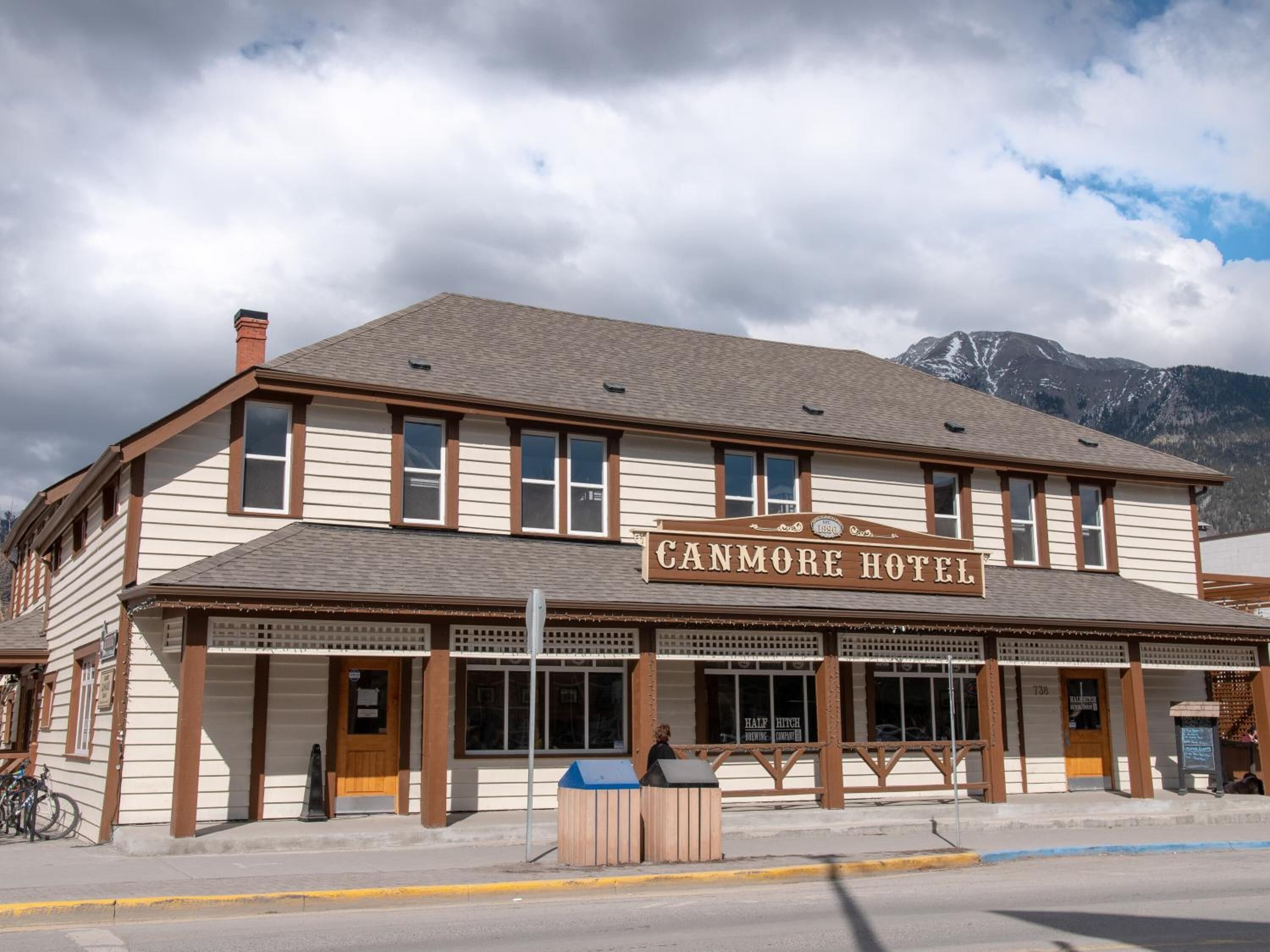 The Canmore Hotel with a traditional architectural style, featuring a prominent sign, large windows, and a view of mountains in the background.