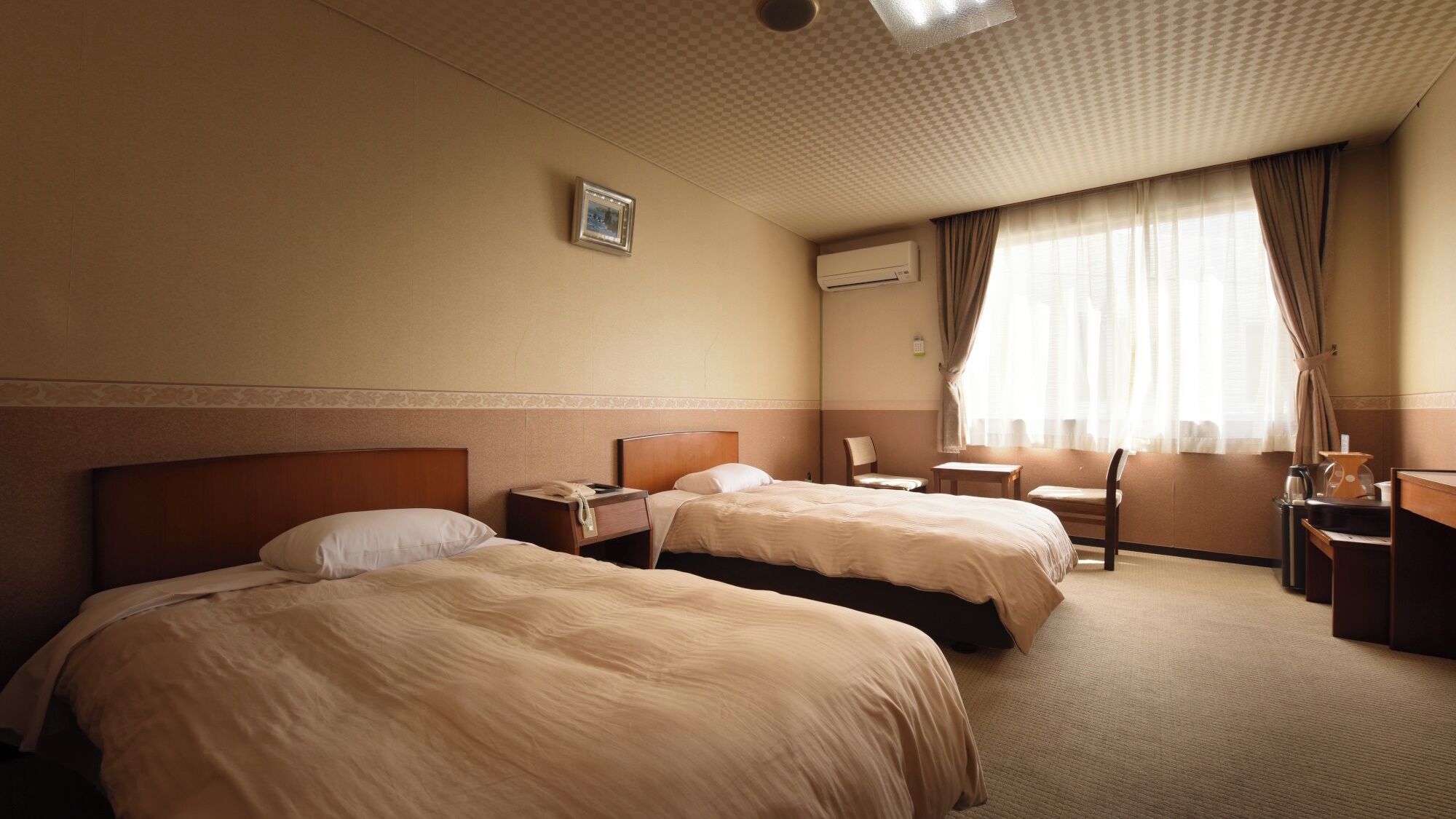 Een hotelkamer met twee bedden, een bureau, een stoel, een tafeltje en een raam met gordijnen.