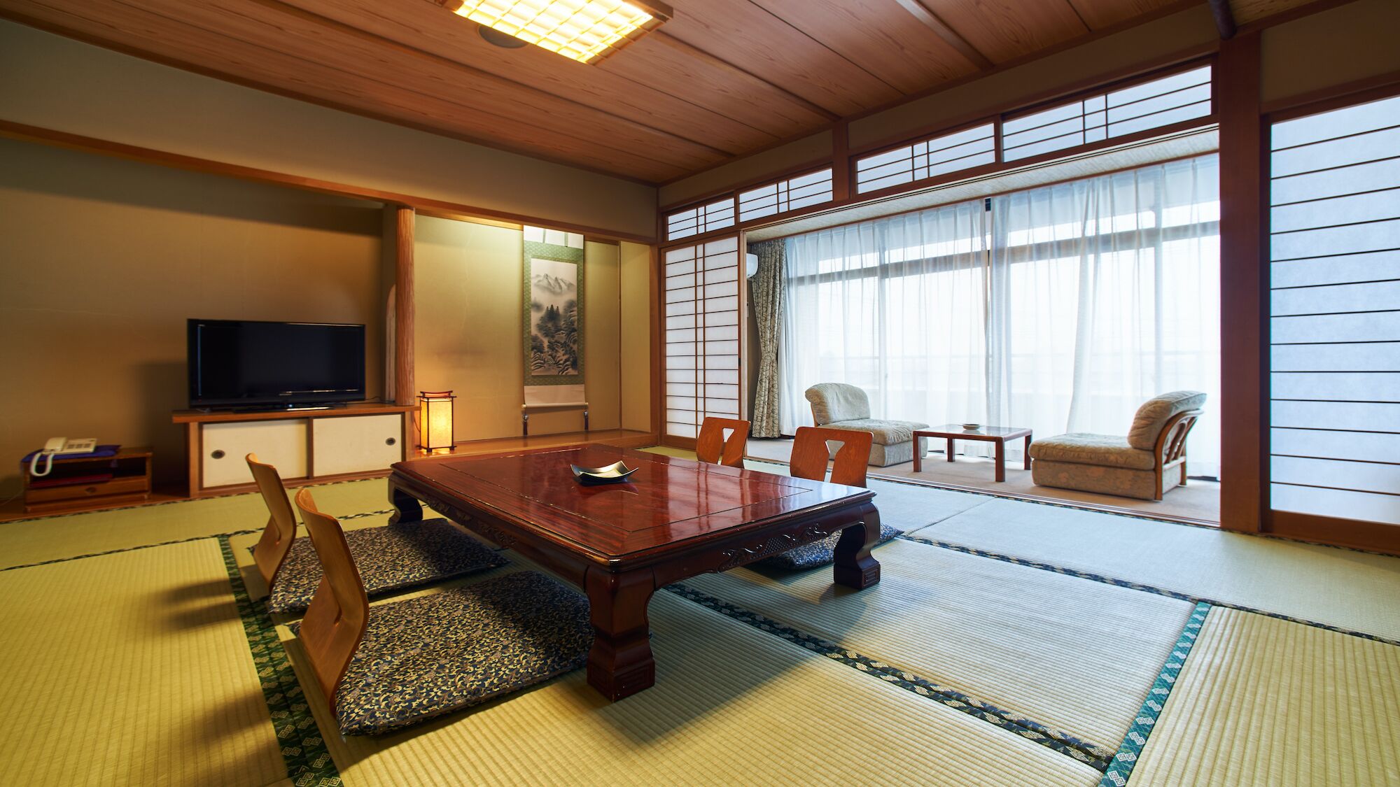 Een traditionele Japanse kamer met tatami vloerbedekking, een houten eettafel, een televisie en schuifdeuren.