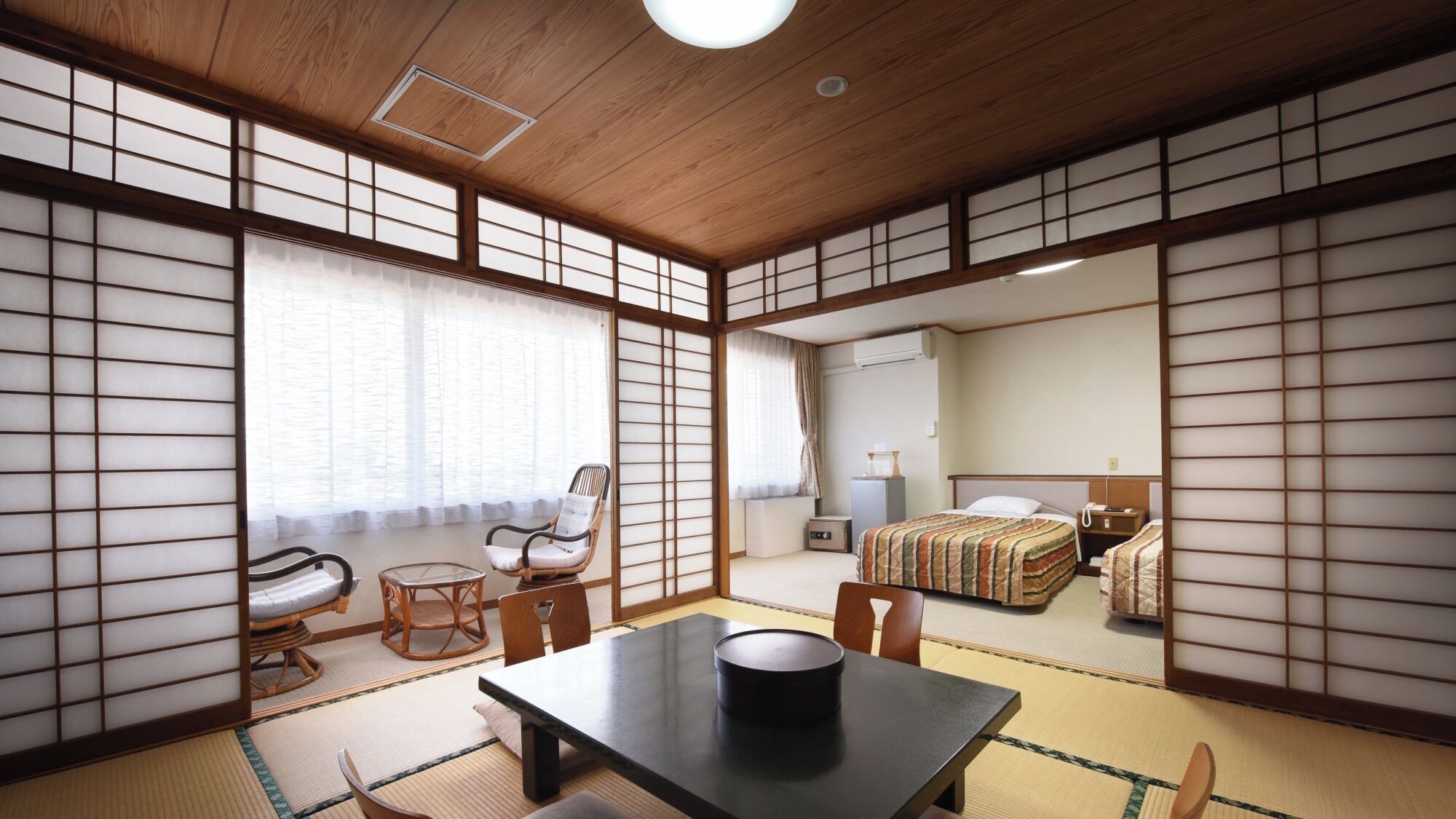 Una habitación tradicional japonesa con suelo de tatami, una mesa baja, una silla, una cama y un escritorio con lámpara.