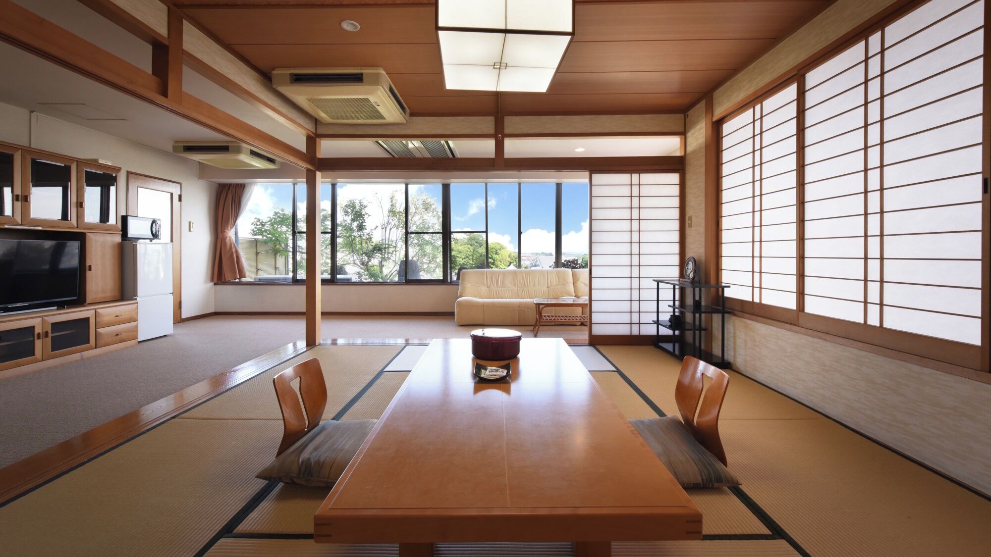 Een traditionele Japanse kamer met tatami vloerbedekking, een lage tafel, kussens, een bank, schuifdeuren en een televisie.