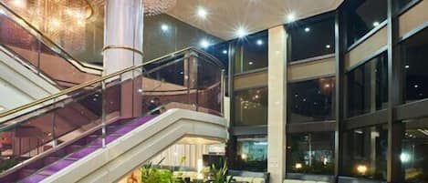 A modern lobby with a central staircase, seating area, and large windows.