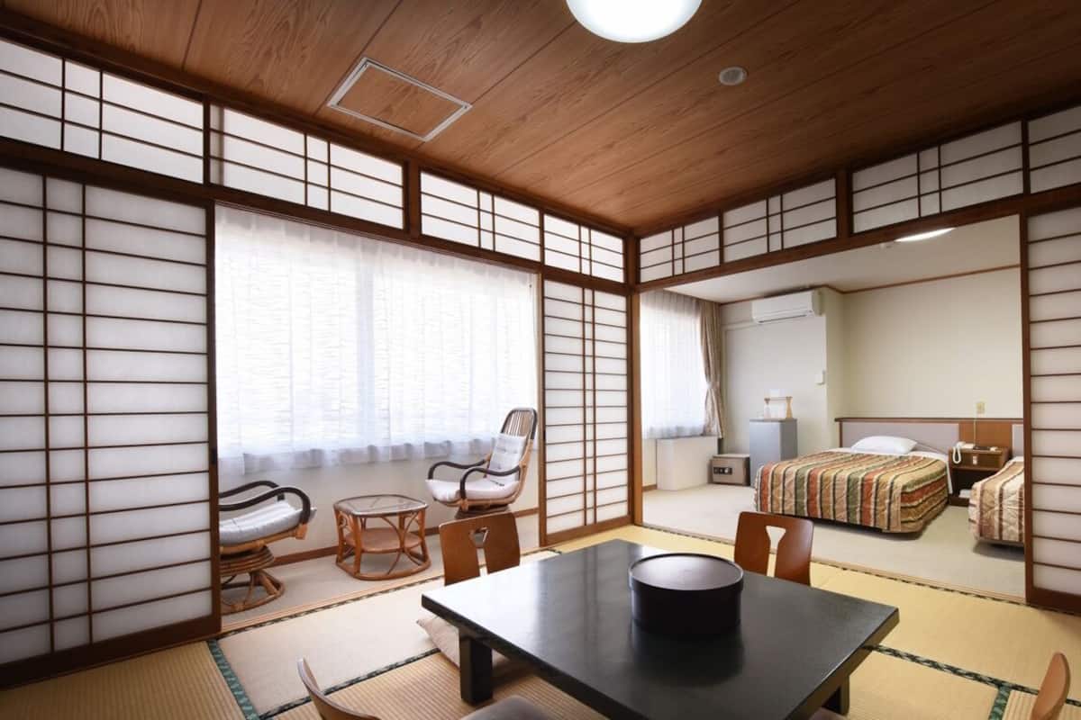 Perinteinen japanilaistyylinen huone, jossa on tatamimatto, matala pöytä, tuoli ja futon-patjalla varustettu sänky.