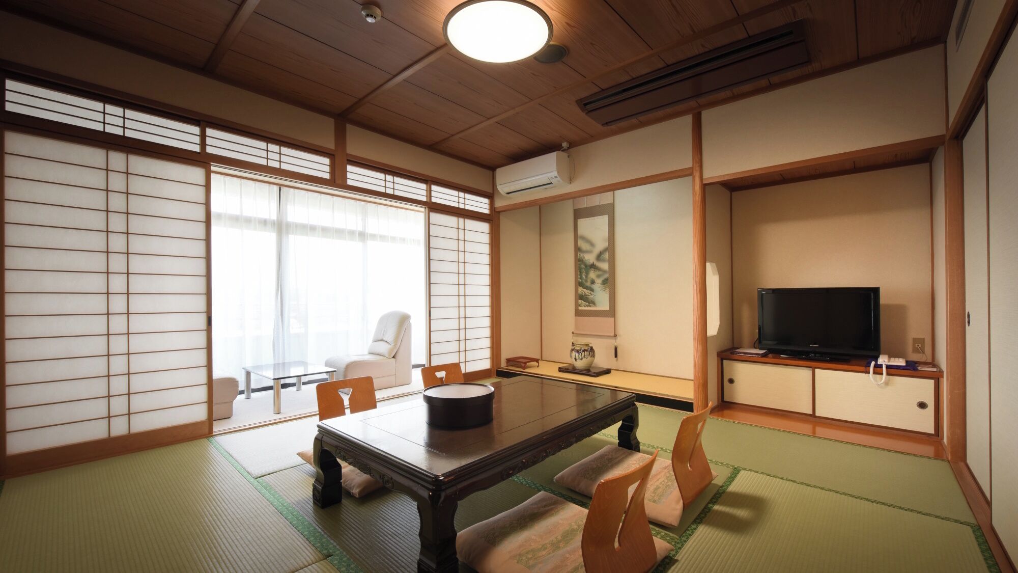Een traditionele Japanse kamer met tatami vloerbedekking, een lage tafel, een bank en een televisie.