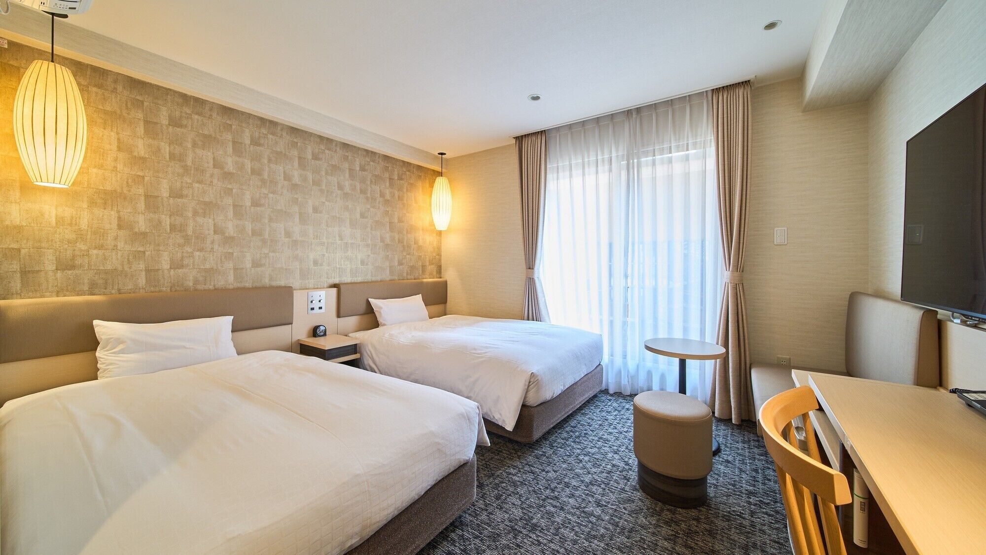 Habitación de hotel con dos camas, un escritorio, una silla, un televisor y una ventana con cortinas.