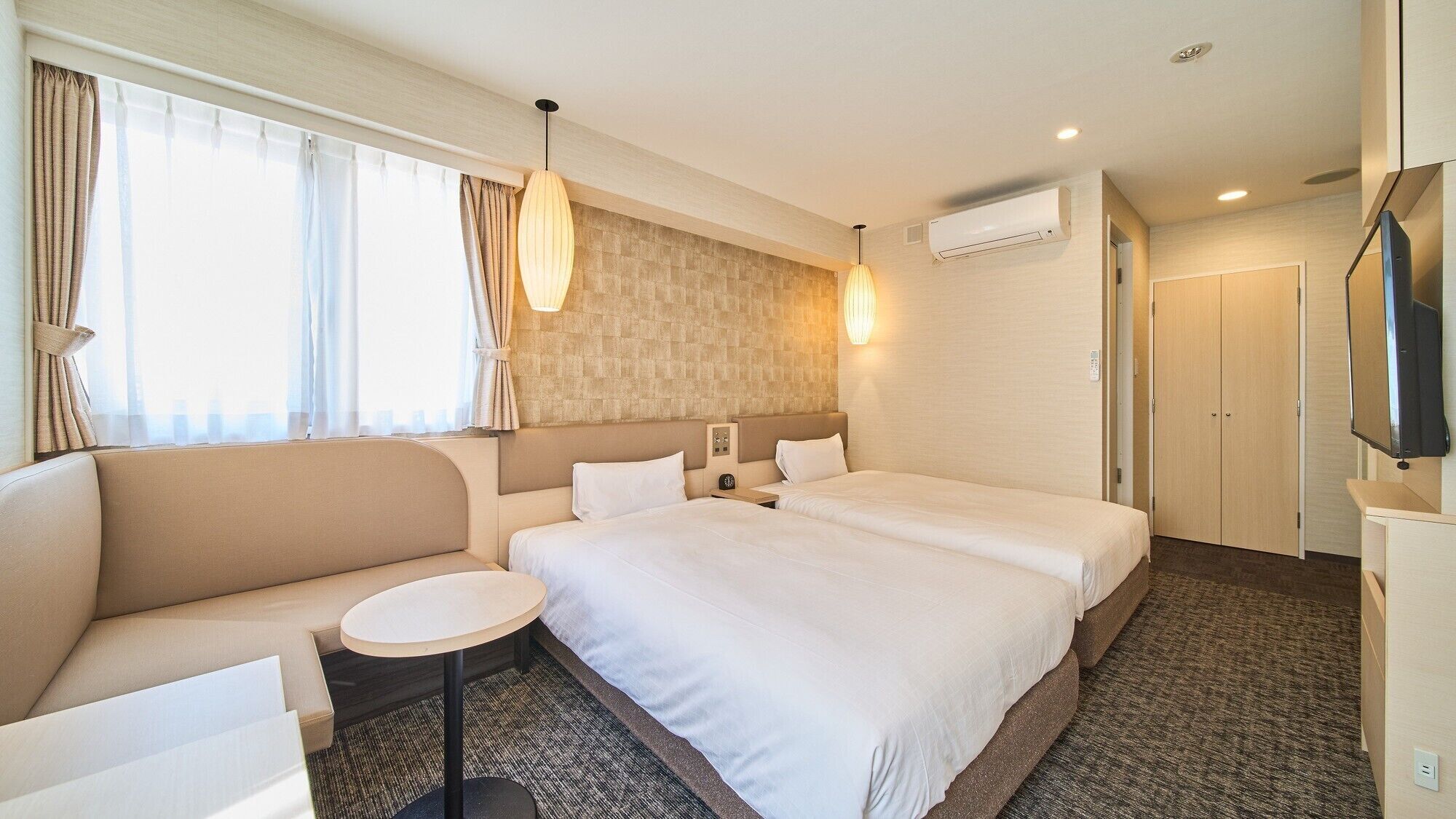 Habitación de hotel con dos camas, un sofá, una mesita, un televisor y aire acondicionado.