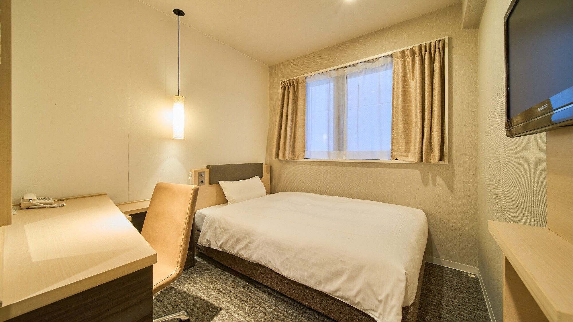 Habitación de hotel con cama, escritorio, silla, teléfono, televisión y ventana con cortinas.