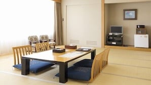 A room with a wooden table, blue cushioned chairs, a television, and a refrigerator.