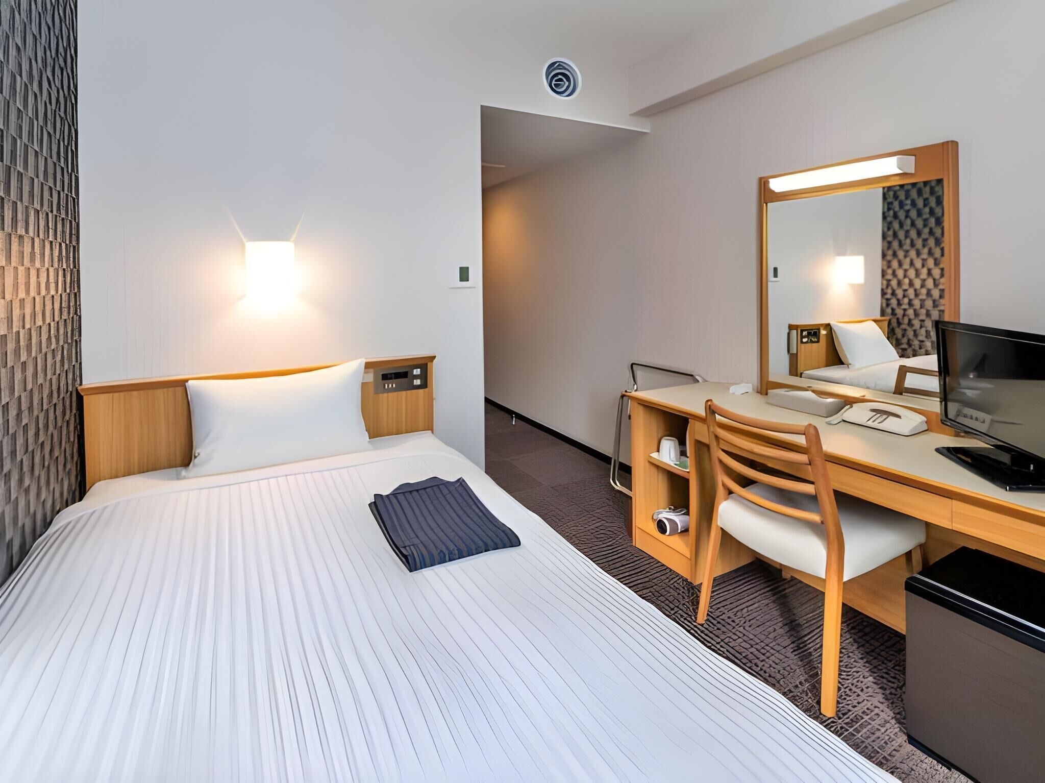 Quarto de hotel com cama, escrivaninha, cadeira e um espelho grande.