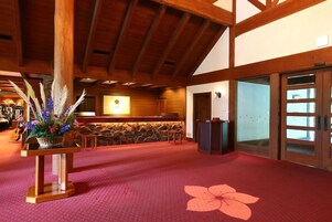 A reception area with a wooden ceiling, a stone wall, a reception desk, and a red carpet with a floral pattern.
