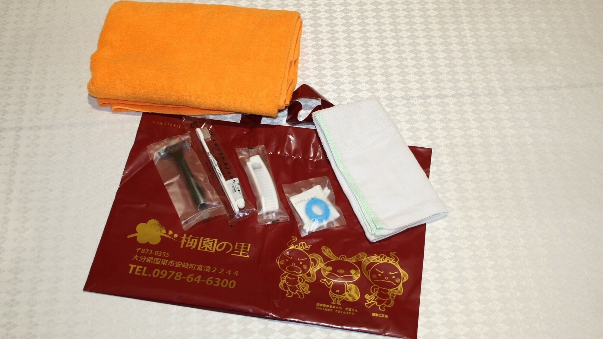 Una tovallola taronja ben arrugada, un borsa vermella amb un emblema daurat, i diversos productes de tocador sobre una superfície amb dibuixos.