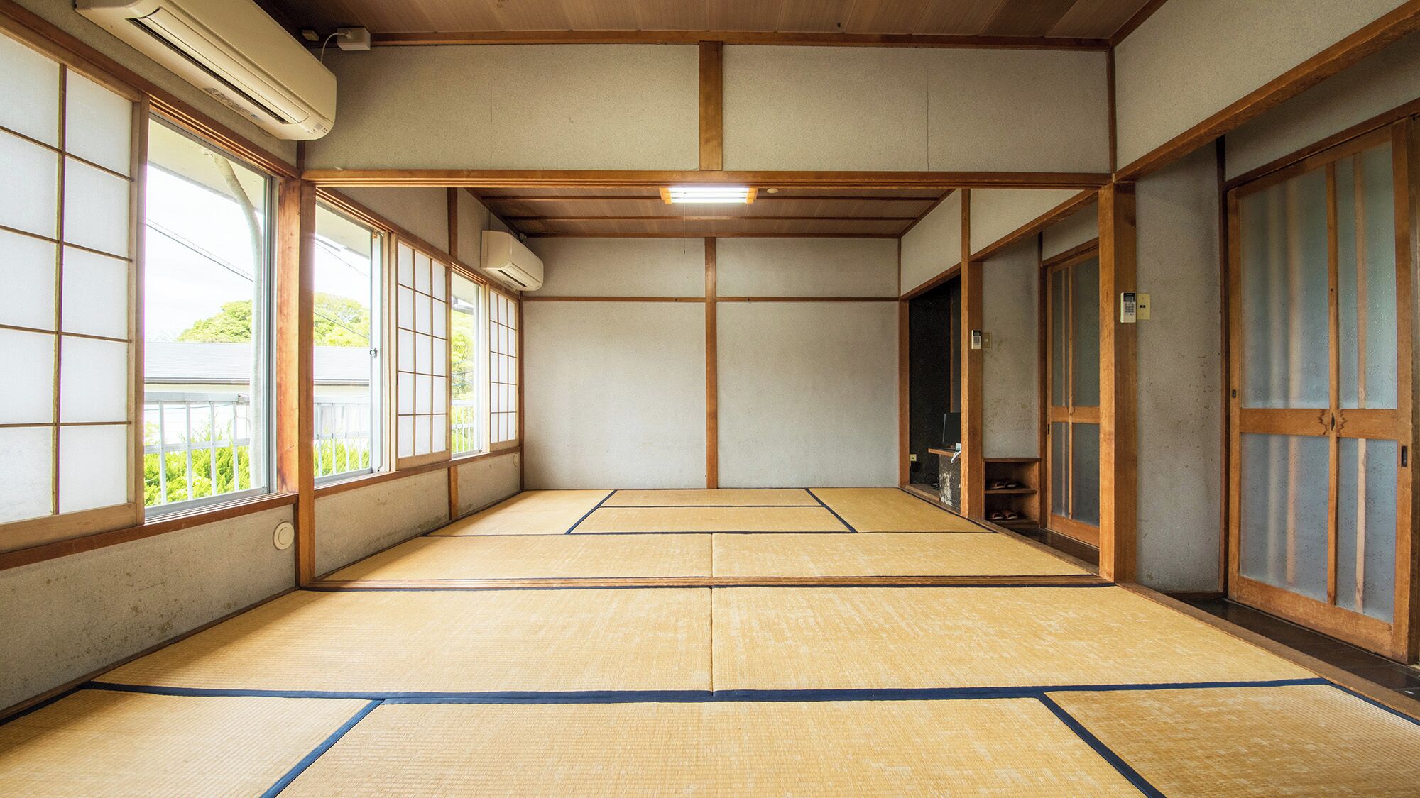 Tatami-mattoilla päällystetty huone, jossa on liukuvat ovet, kattotuuletin ja näkymä ikkunoista.
